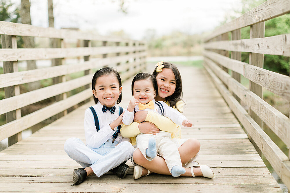 3 kids smiling sitting on the bridge in Prince William County, Virginia
