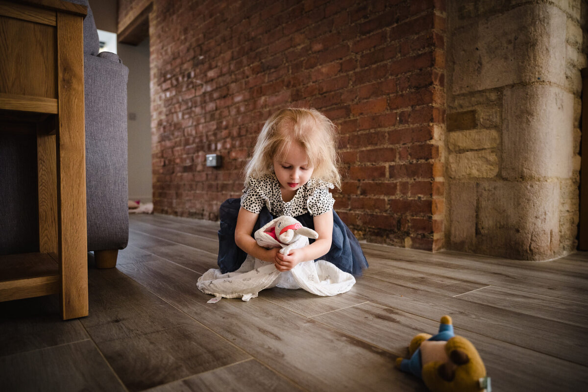 Little girl sat on the floor at home playing with teddy amanda forman photography