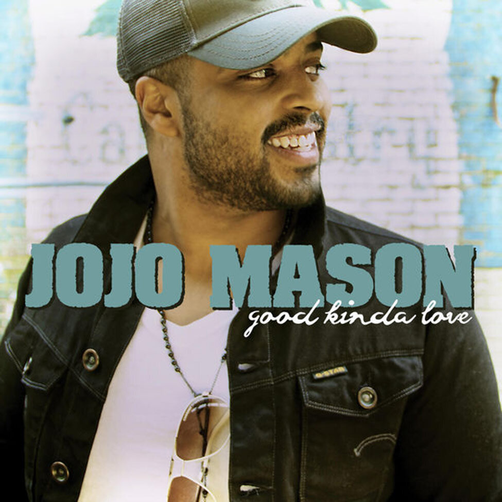 Single Cover Title Good Kinda Love Artist JoJo Mason Singer smiling while looking voer his shouler white and blue brick wall behind him wearing baseball cap and sunglasses hanging off chain around his neck