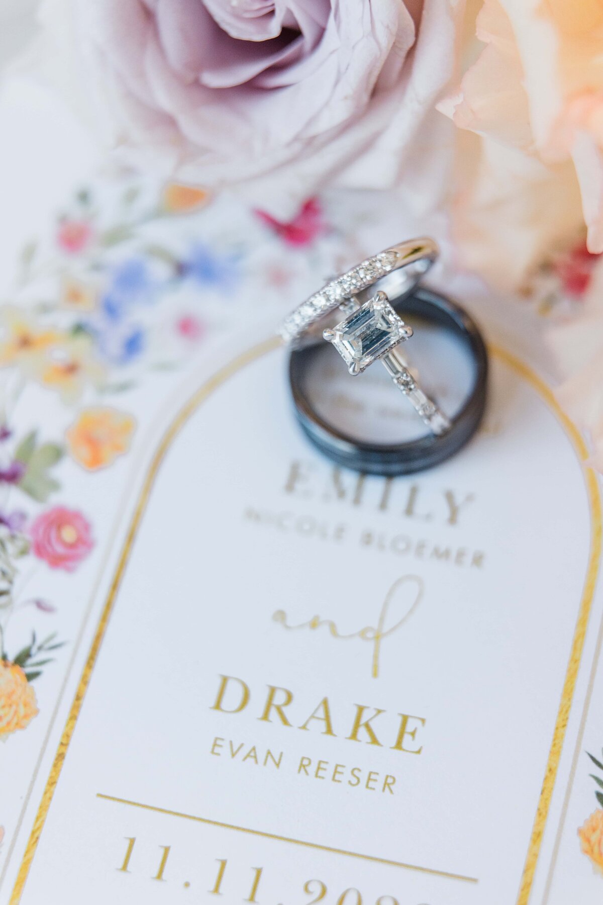 Close-up of an engagement ring on a floral wedding invitation with names "Nicole Bloomer and Drake Evan Reeser" and date "11.11.2029", coordinated by a renowned wedding