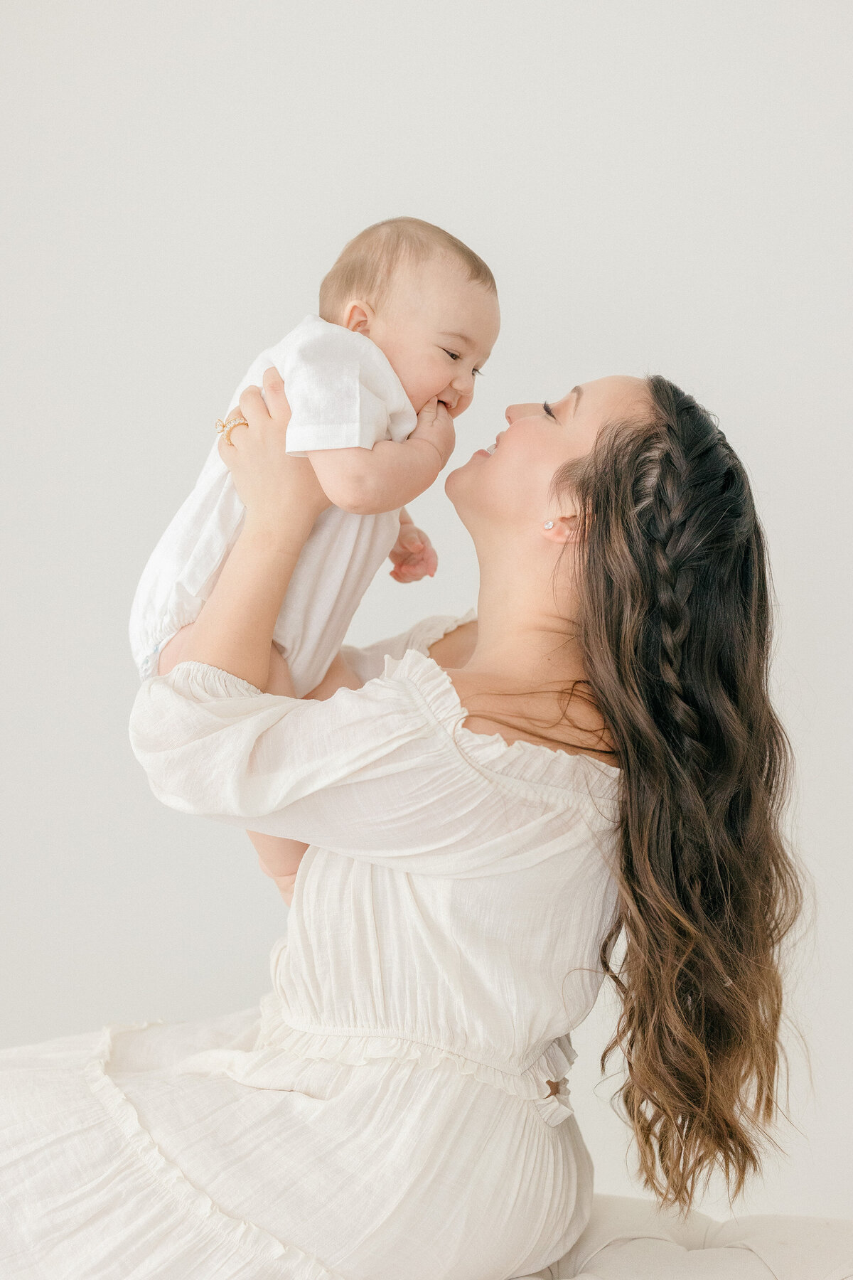 A mom holding up her son smiling at him in all white studio by NJ Newborn Photographer