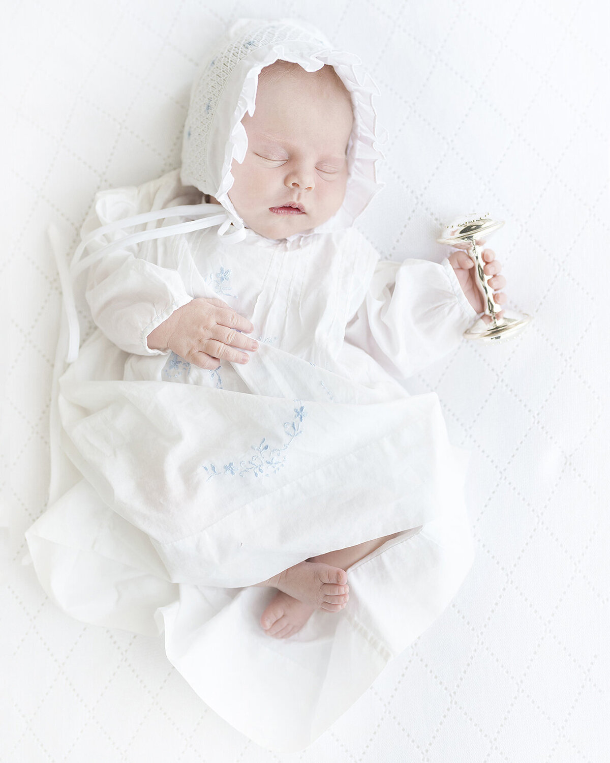 newborn baby in a grandmillenial style feltman brothers dress with a silver rattle