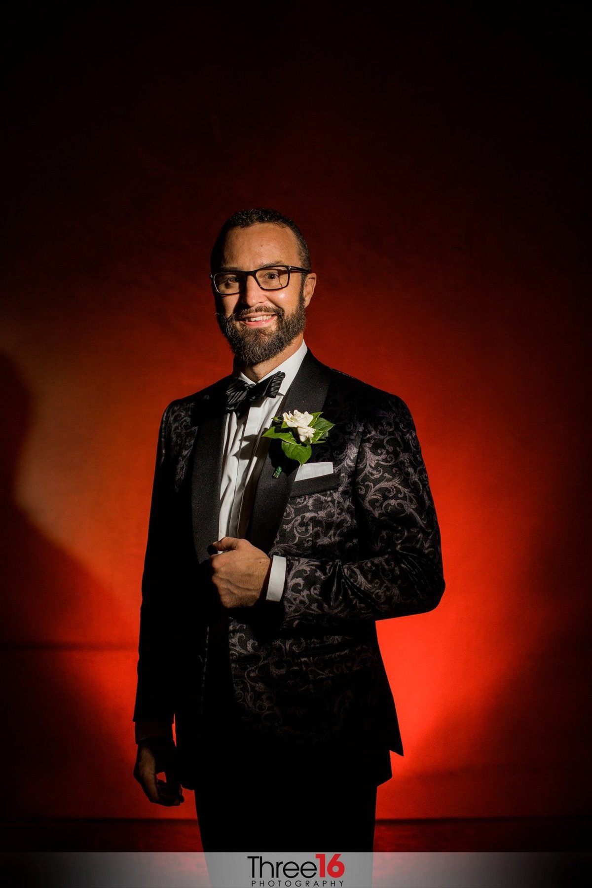 Groom poses with a red backdrop behind him