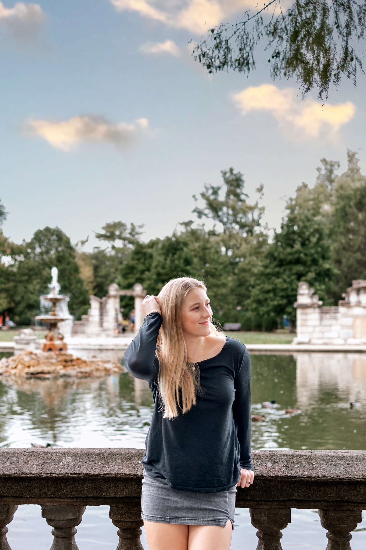 A beautiful young lady is leaning against a concrete rail  in Tower Grove Park for her Senior photos.