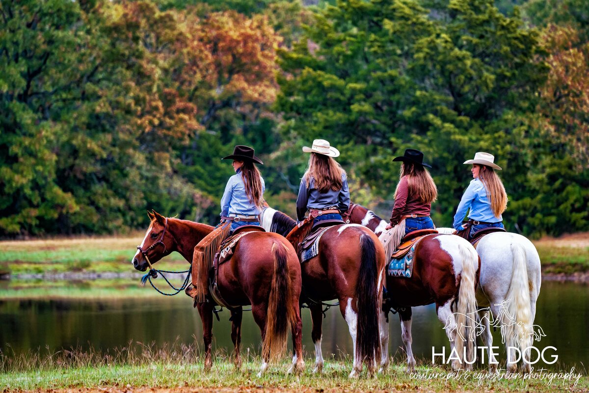 Four female equestrians wearing western attire sit on their horses facing away from the camera at a lake in Northern Texas.