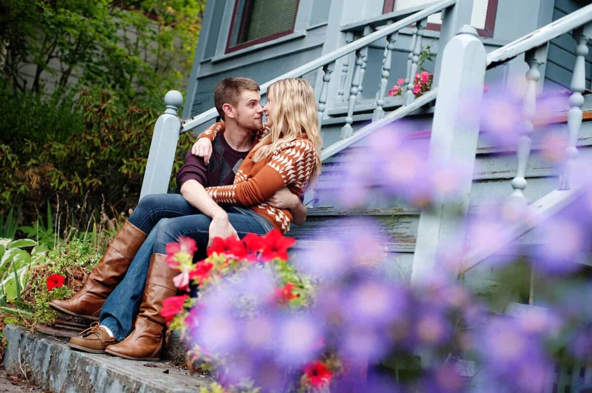 a woman sits on a mans lap on blue stairs surrounded by spring flowers