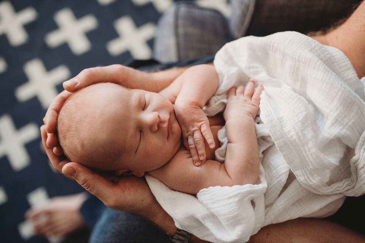 Man's hands cradling newborn head in nursery in Baltimore Maryland