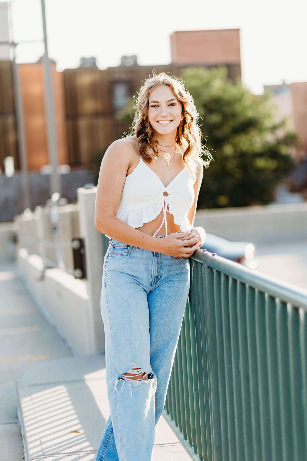 High School Senior girl leaning against a raining on top of a parking garage.