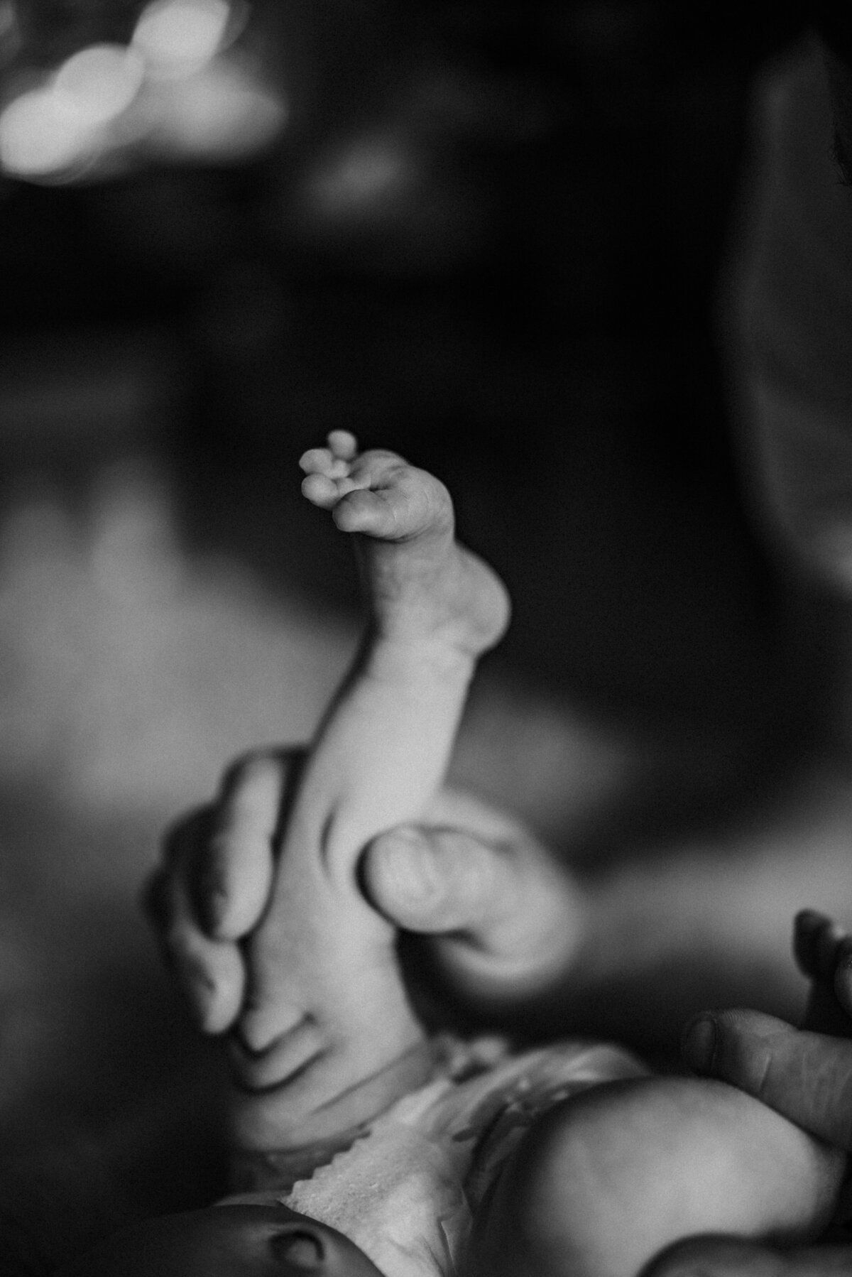 Newborn baby leg and foot being held up by dad