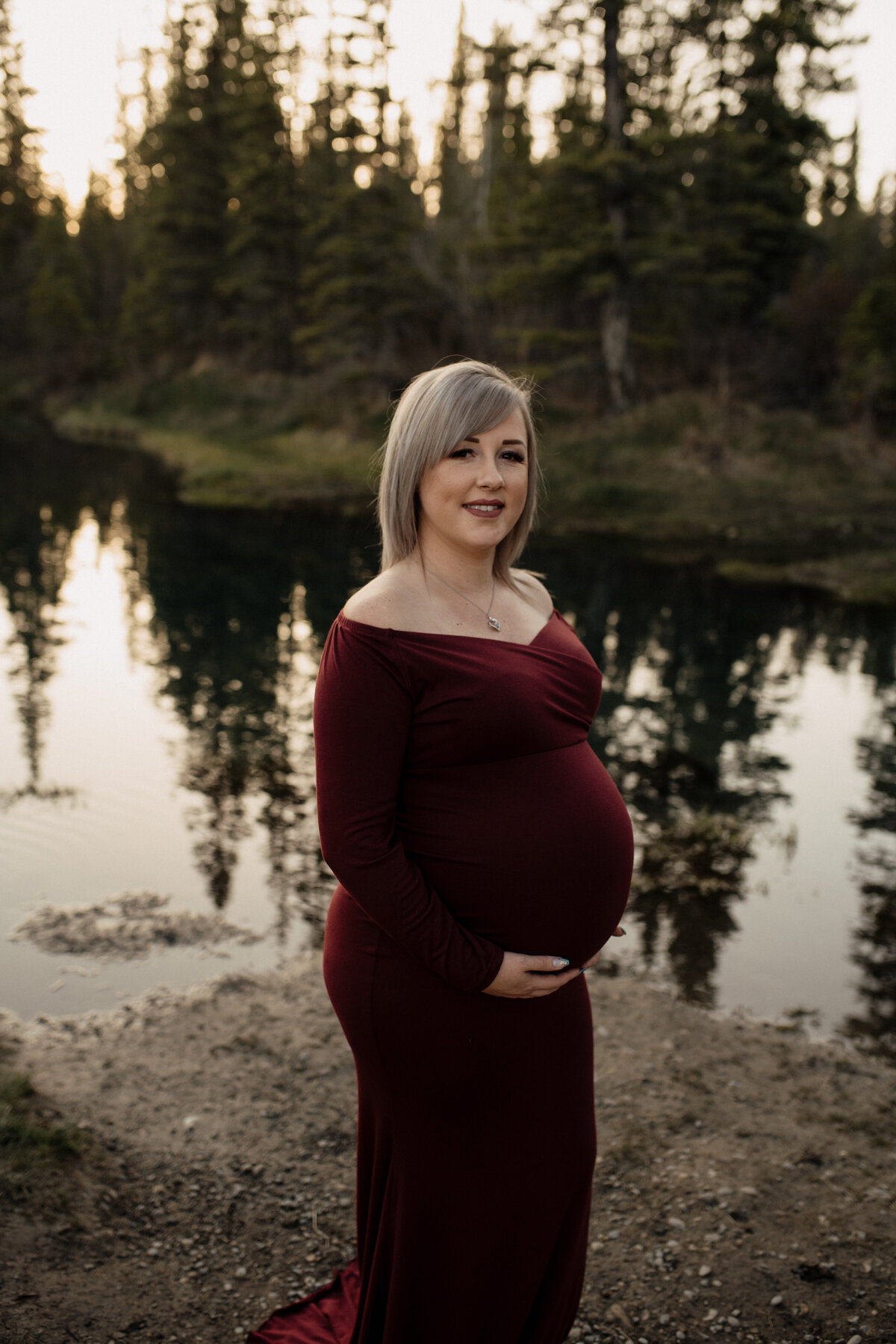 Pregnant woman in red dress in front of lake
