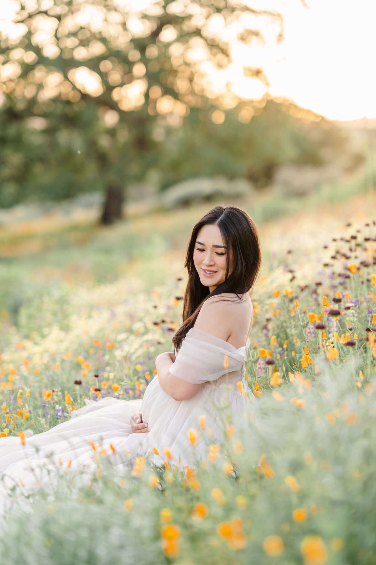 A maternity session photographed by Bay Area Photographer, Light Livin Photography shows an expecting mother sitting and caressing her baby bump in a field of poppies.
