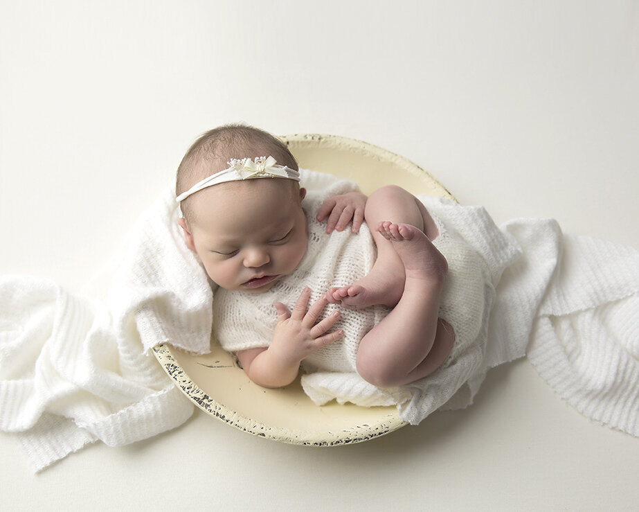 newborn baby girl in white outfit posed in white bowl sleeping for Greensburg photography session