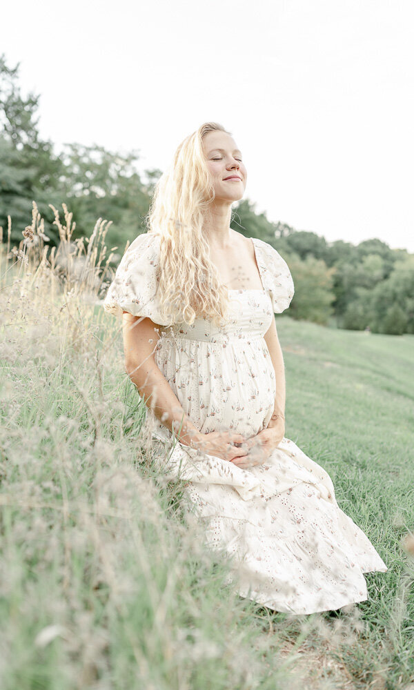 Pregnant woman sits in a field of tall grass at sunset
