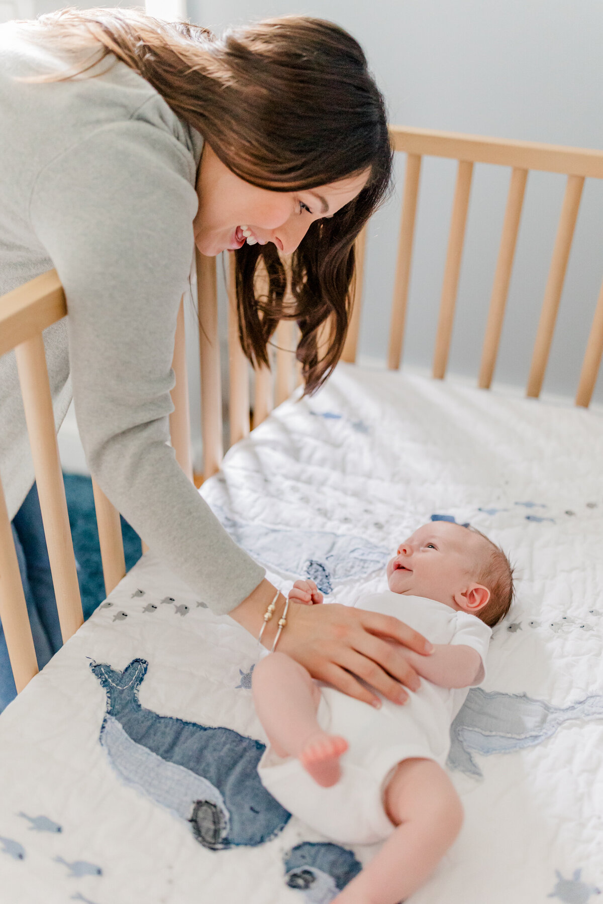 Smiling mother leaning over crib with her hand on smiling newborn baby's tummy