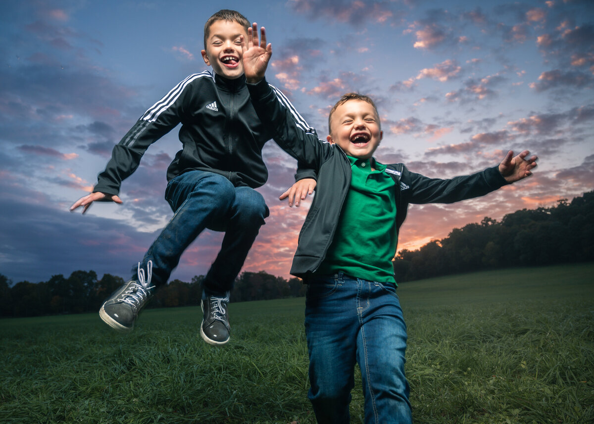 Two boys laughing and jumping toward camera at sunset, fun not posed picture