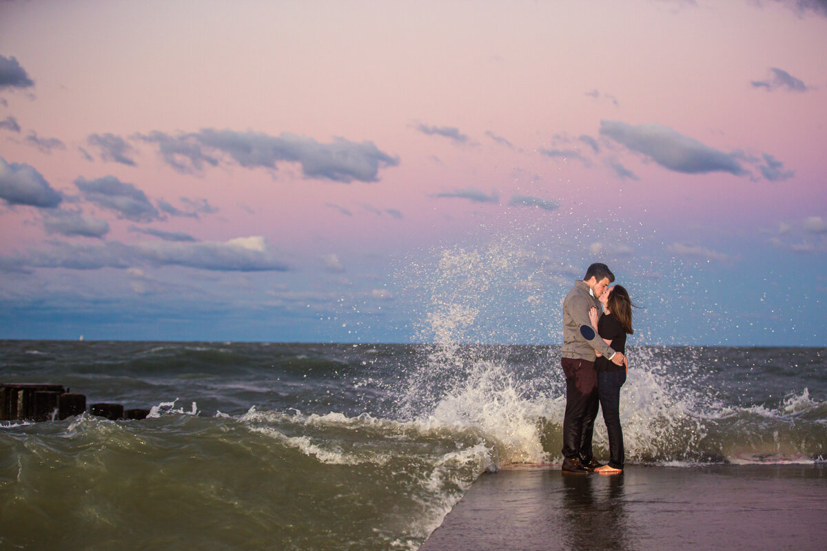 Waves crash over a couple taking sunset engagement photos in Chicago