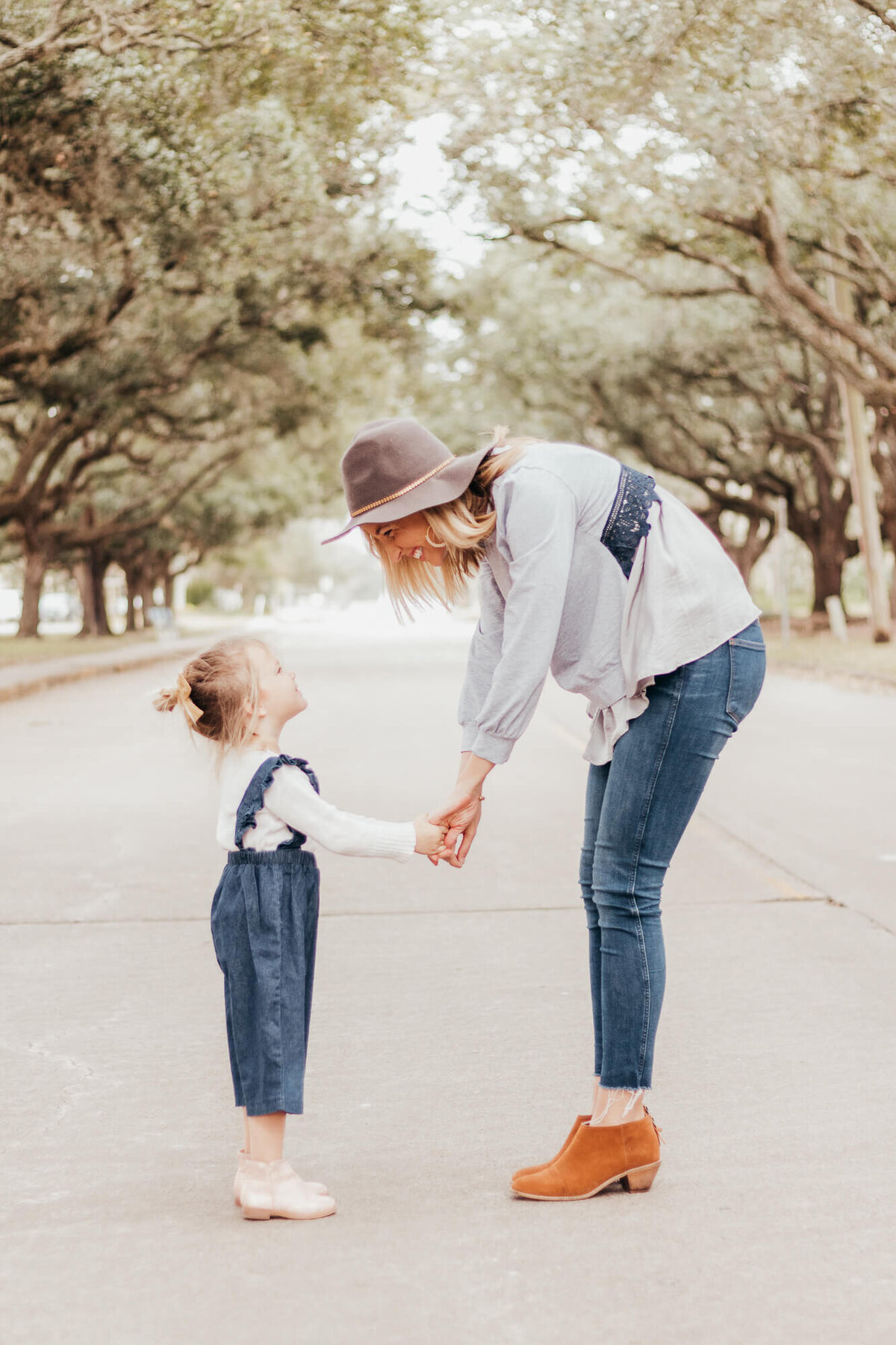 Mom and daughter hold hands and look very lovingly up at each other while standing under arched oak trees.