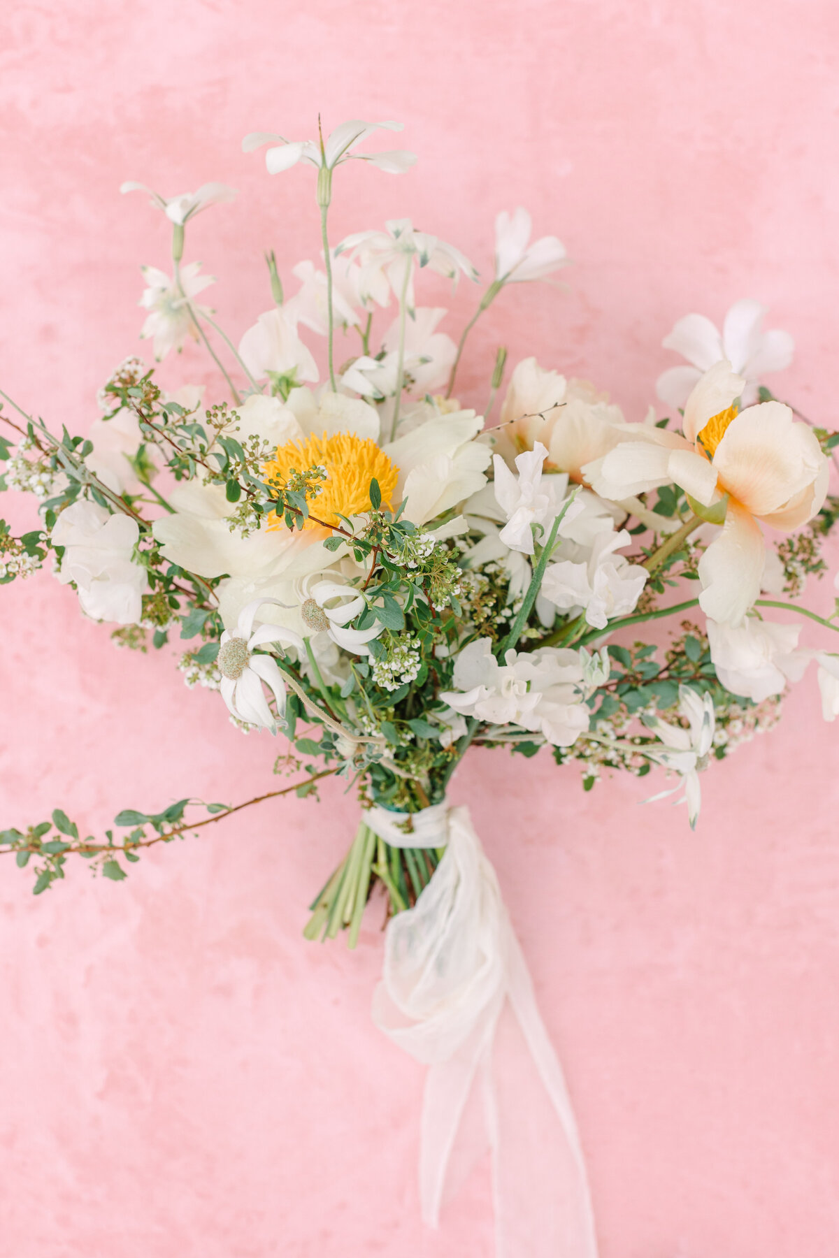 white and orange bridal bouquet with loose greenery on pink backdrop.