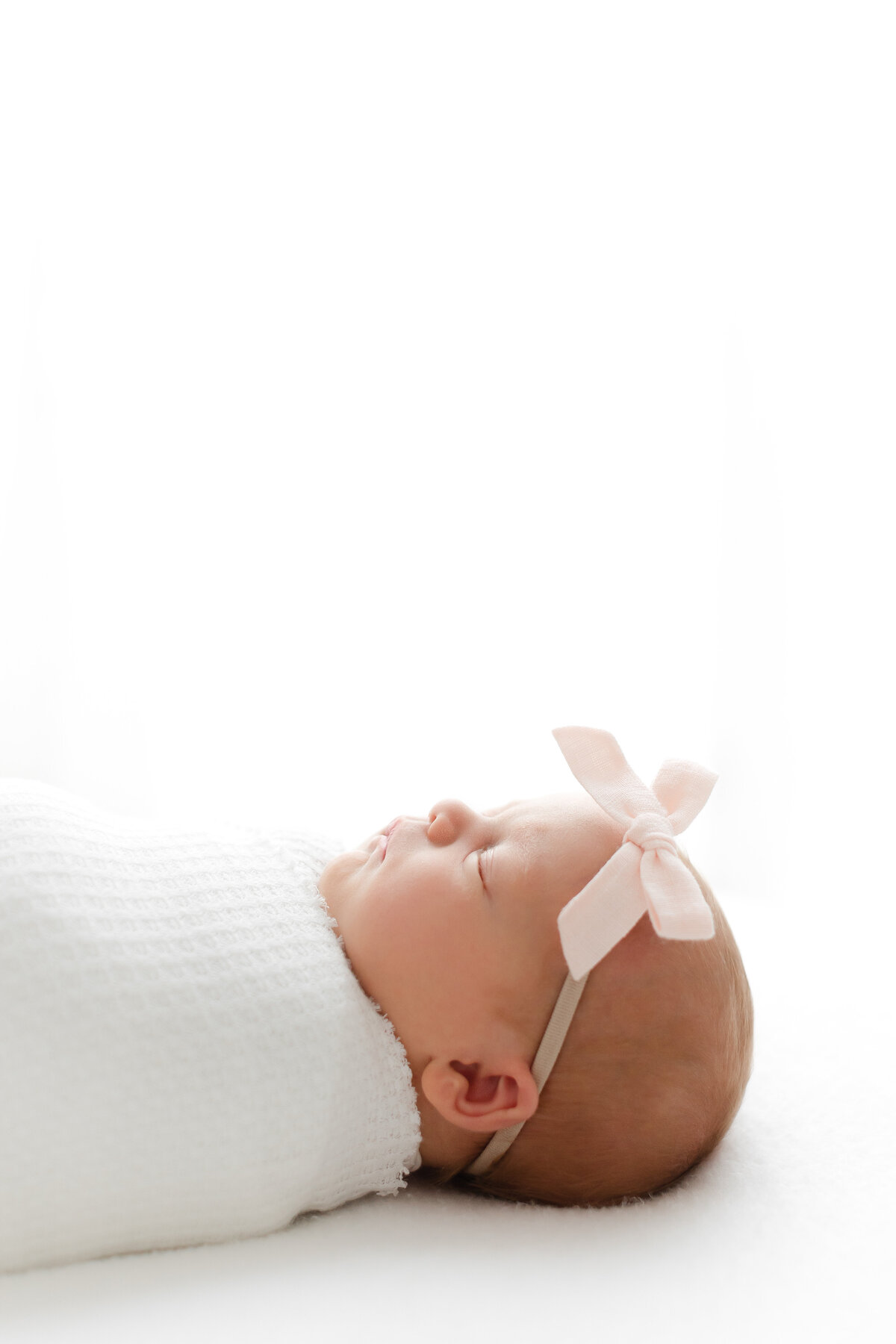 A profile photo of a newborn baby girl swaddled wearing a pink bow at her DC Newborn Photography photoshoot