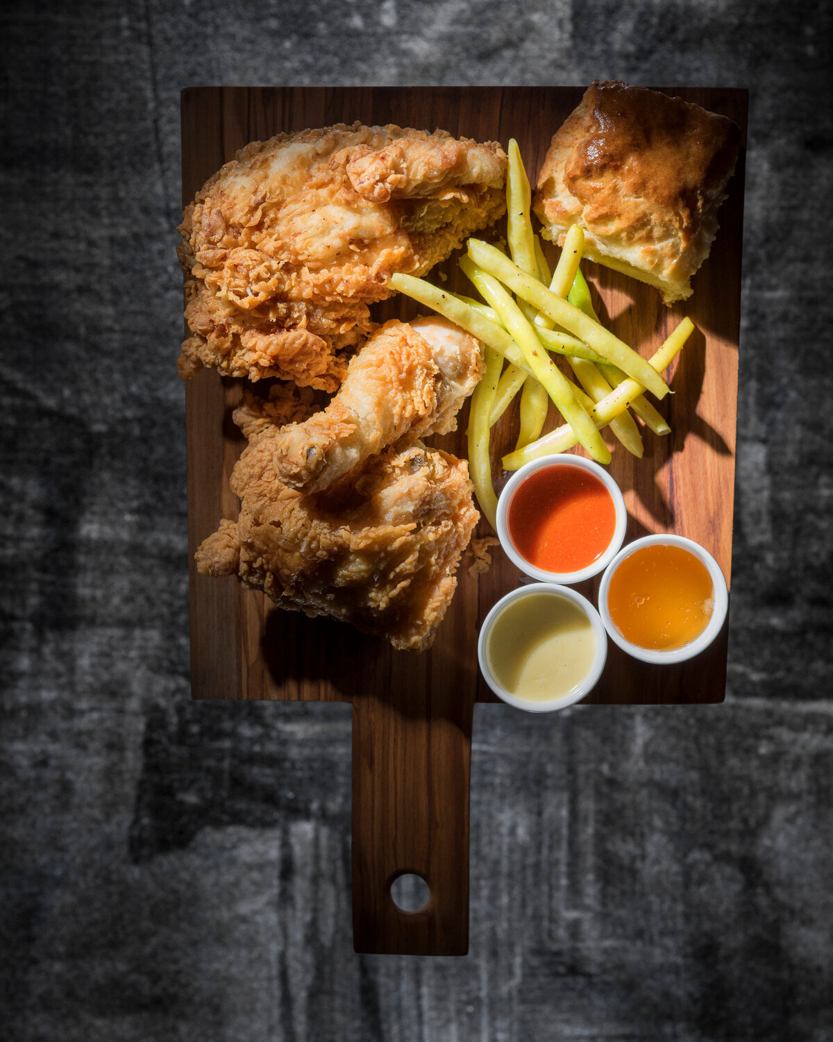 Fried chicken, fries, and sauces on a wooden plate