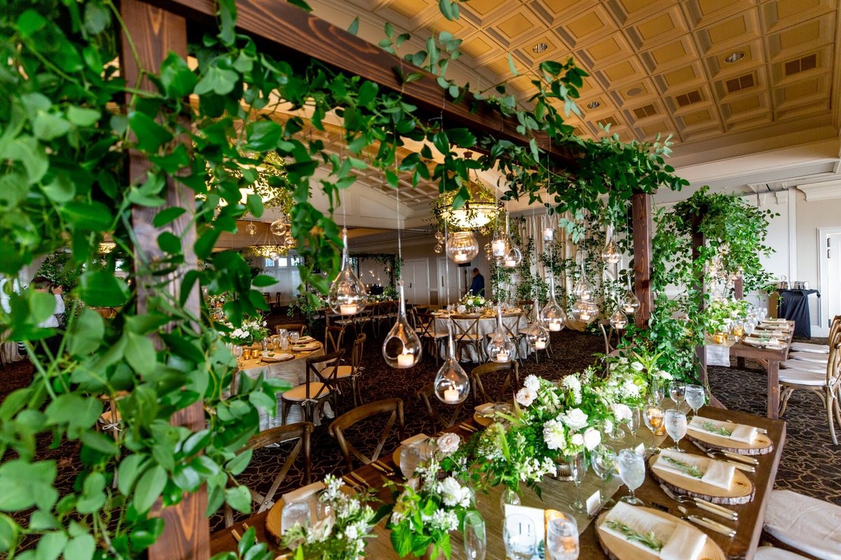 wooden farm table decorated with greenery centerpieces and wooden trellis with hanging candles
