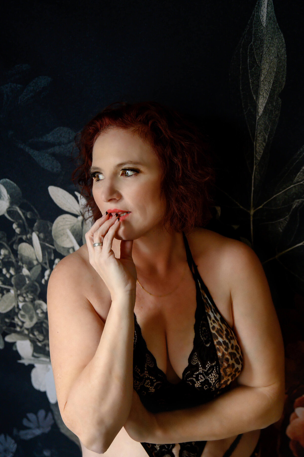 Woman sitting in front of a floral background in a leopard lingerie with her fingers in her mouth