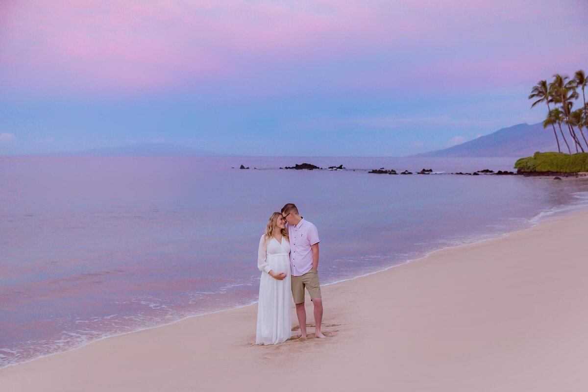 Couple wearing white look at one another while being photographed for their beautiful maternity vacation in Hawaii