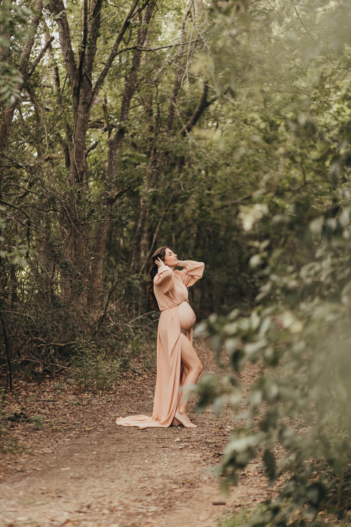 standing behind a tree, a mother pregnant with baby boy, holds her hair.