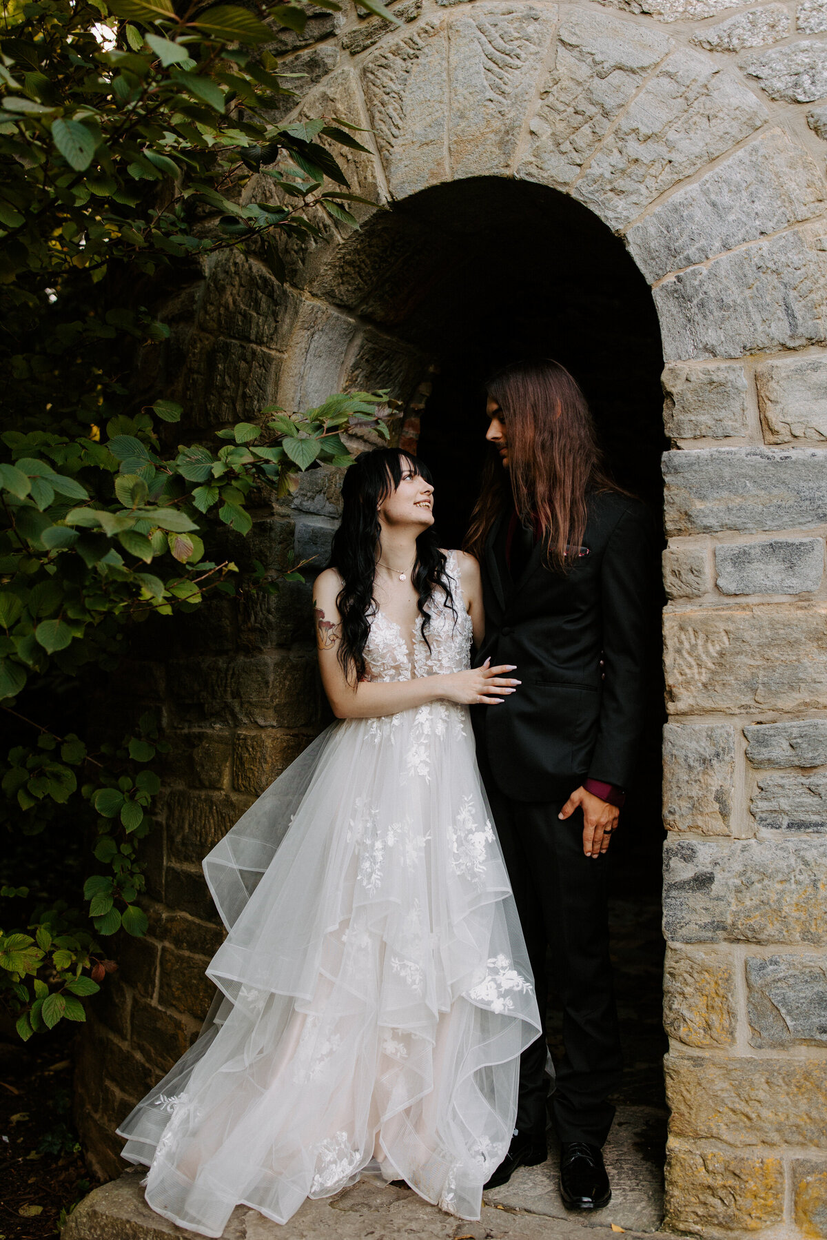wedding couple standing next to each other smiling in a small archway