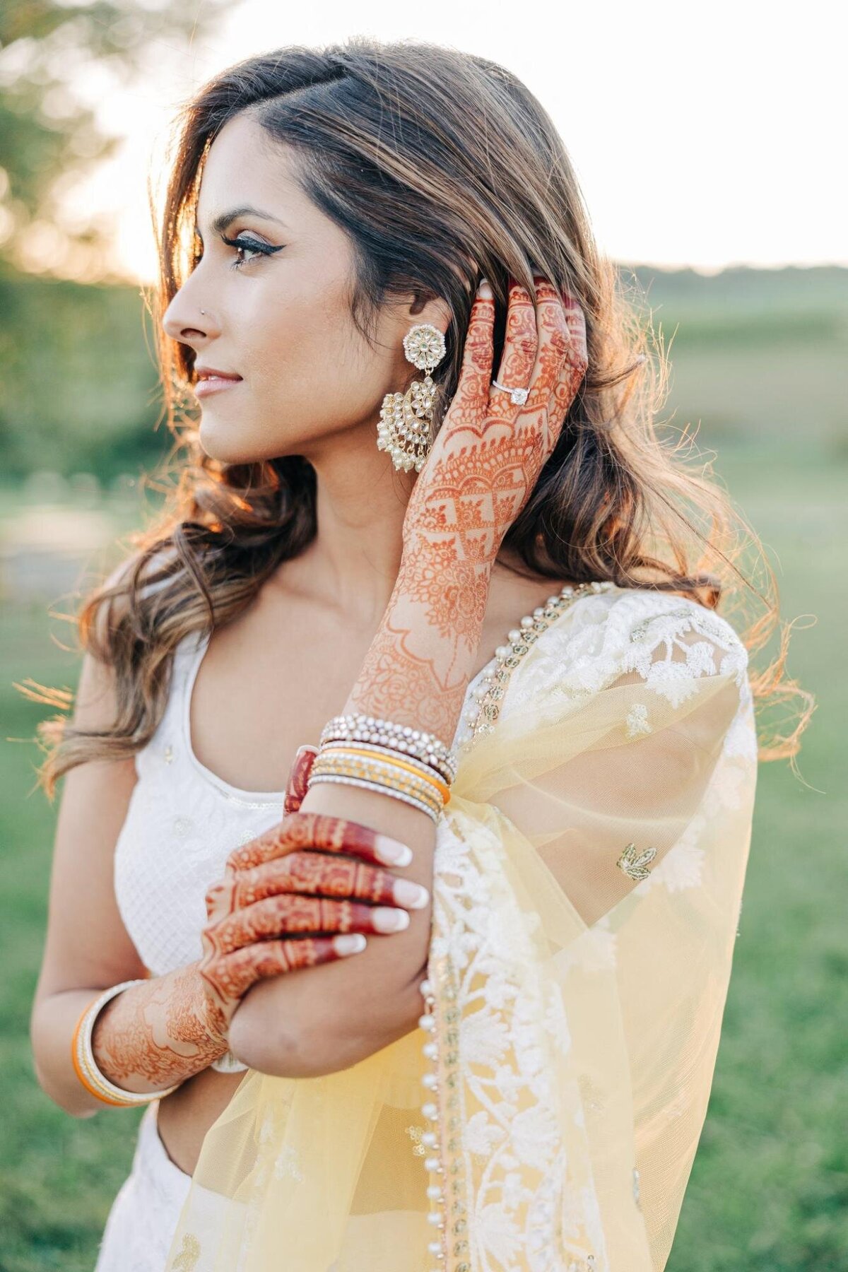 A woman adorned with henna and traditional jewelry looks away pensively.