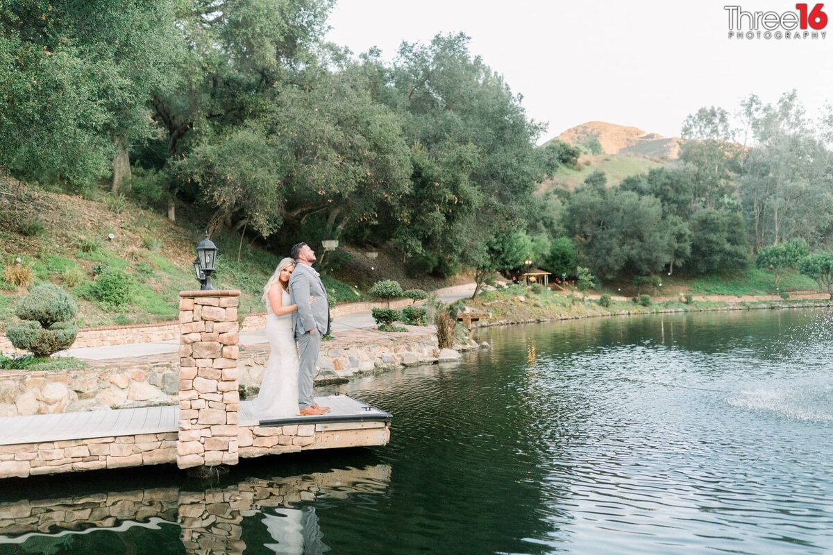 Groom looks out over the lake while his Bride embraces him from behind