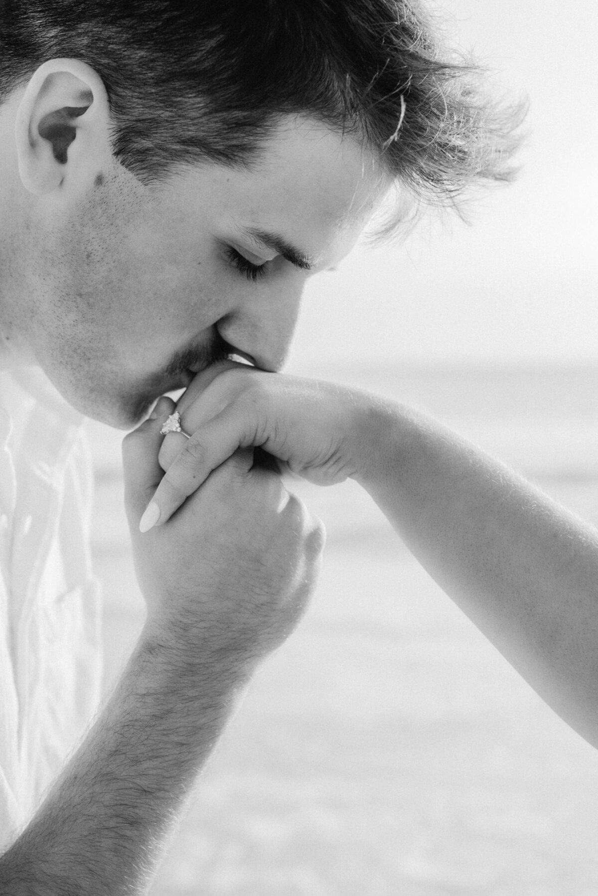 B&W shot of man kissing newly engaged fiance's hand/new engagement ring