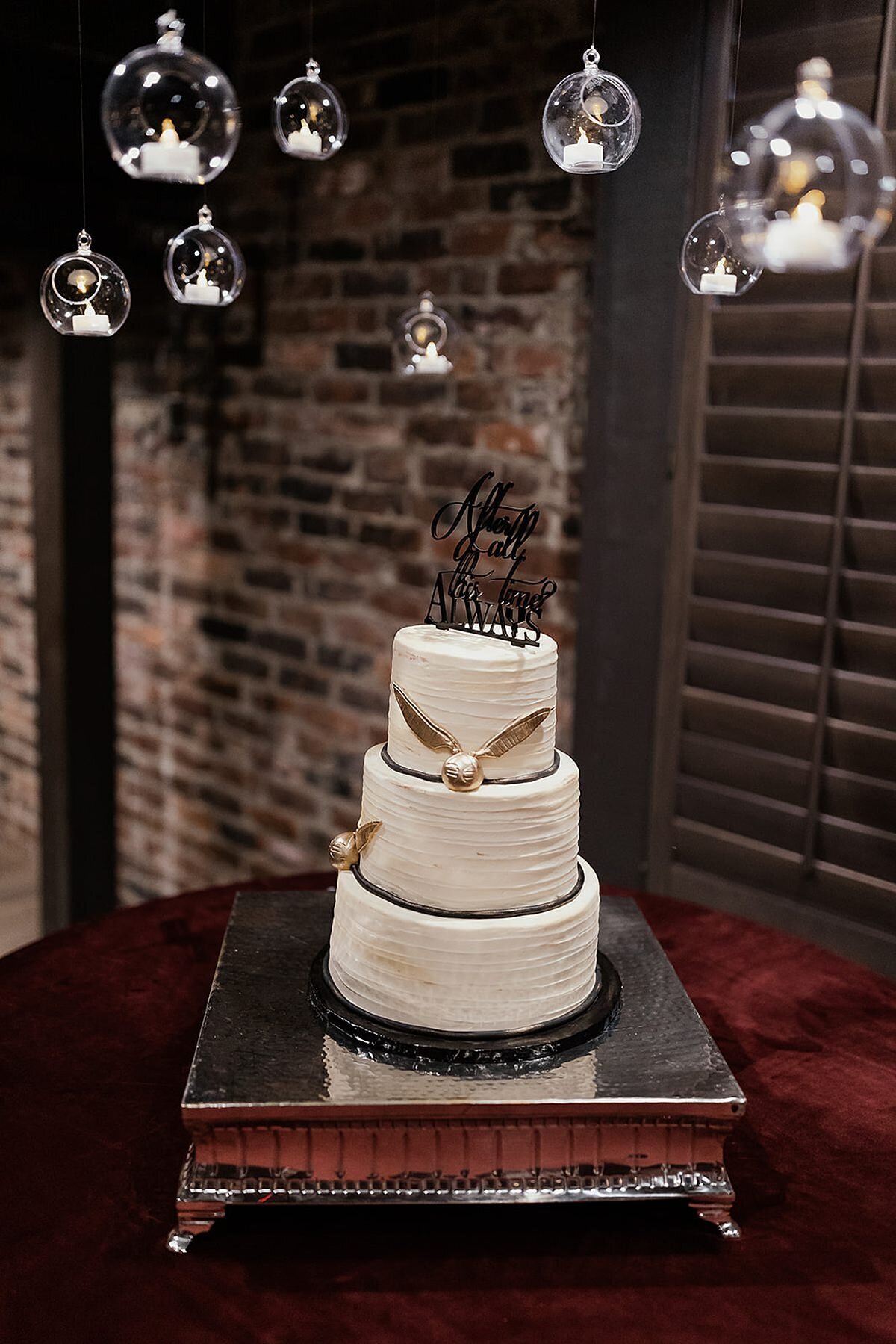 "After all this time, always." white three tier wedding cake with two golden snitches sits on a square silver cake stand with glowing snitches hovering in the air above the cake at The Bedford Event Center in Nashville.