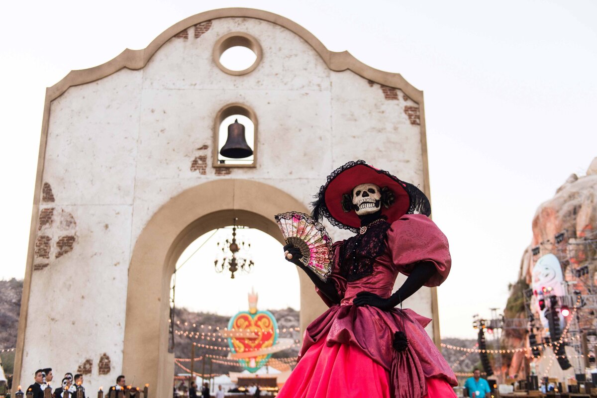 Day of the dead entertainer with fan in front of entryway with bell welcomes attendees to an offsite party at incentive travel event