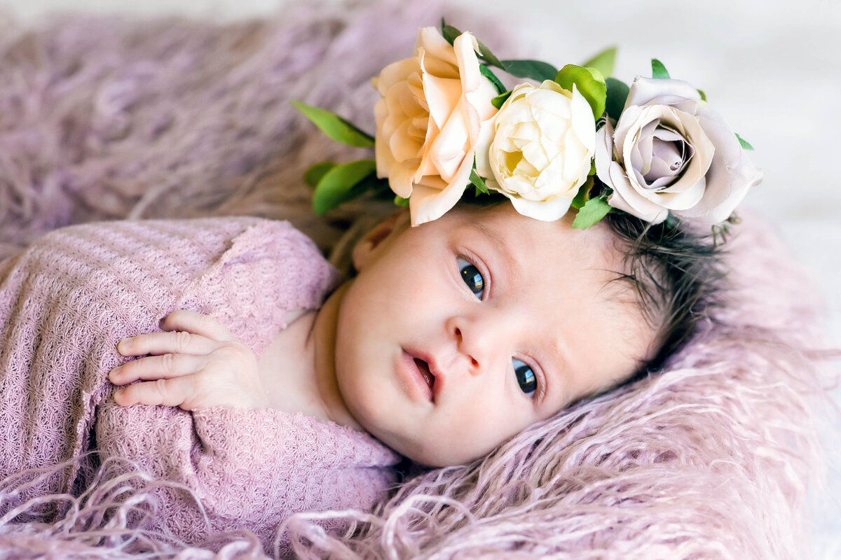 in home newborn session of  a  baby girl wearing lilac wrap with a flower crown  with her eyes open