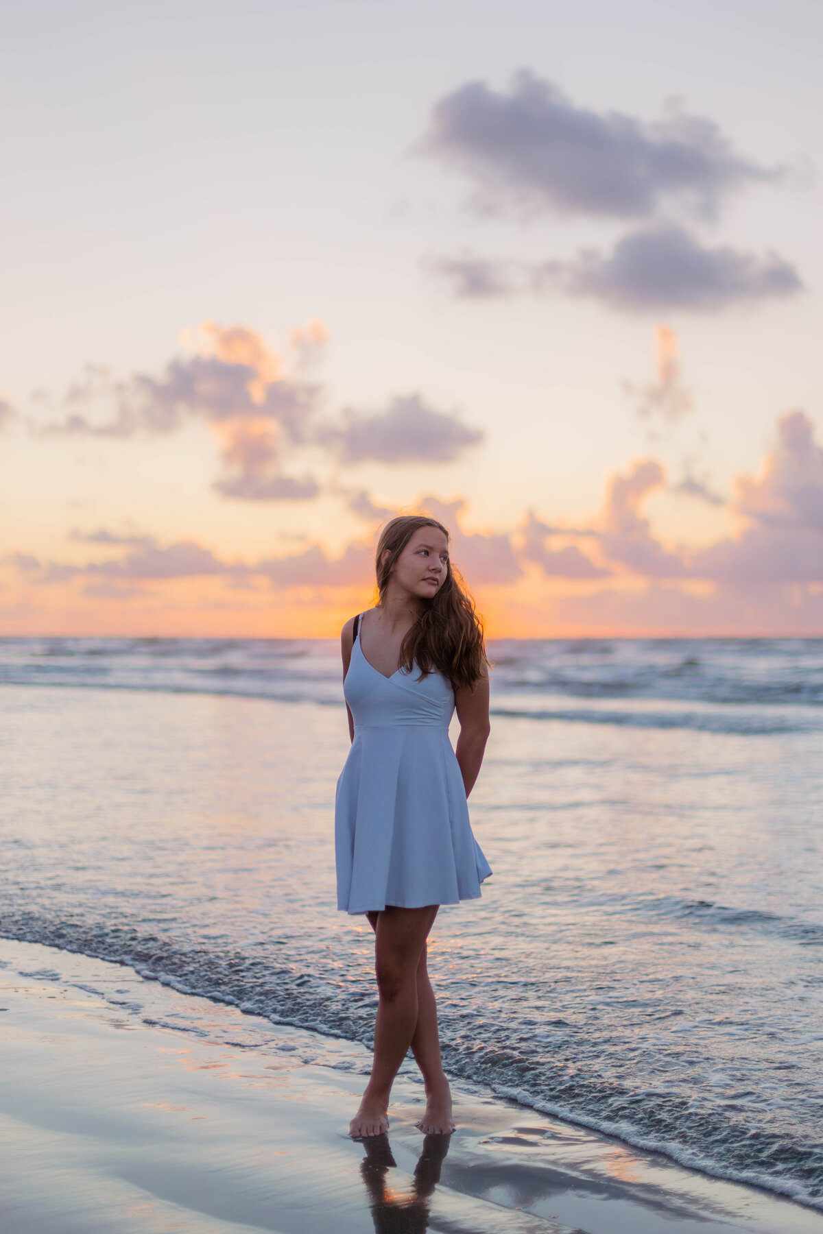 A girl stands on the beach at sunrise in Galveston Texas surrounded by pink and orange skies