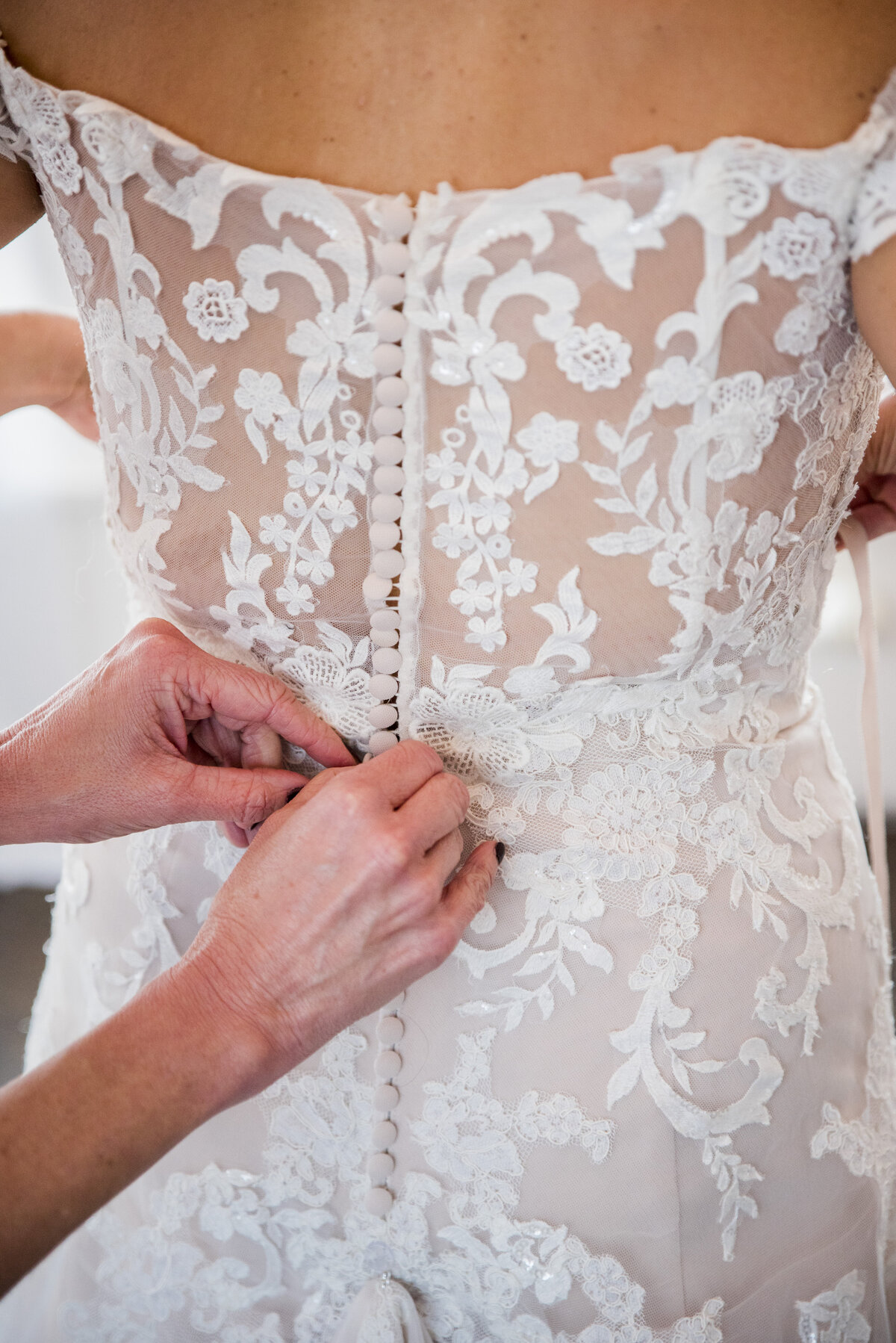 A close up shot of a bridesmaid's hands buttoning a lace wedding gown on the bride.