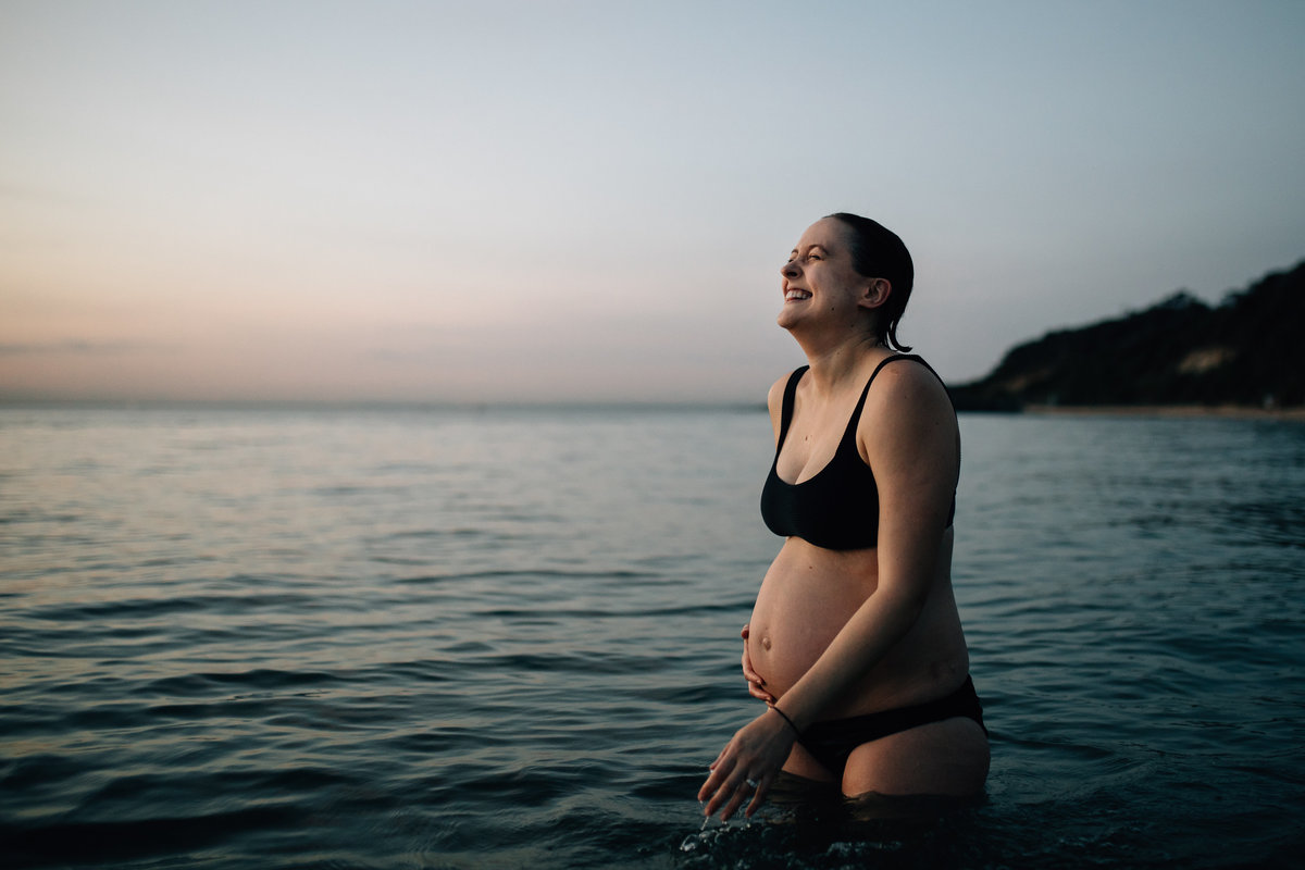 pregnant woman in black bikini laughing while standing in ocean at Melbourne beach