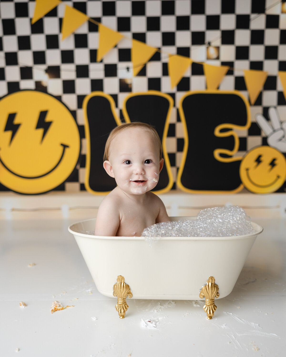 Adorable little one wrapping up their cake smash with a bubbly soak in their own mini hot tub smiles, suds, and all! Captured by Yucaipa cake smash photographer Kaitlyn Dawn Photography.