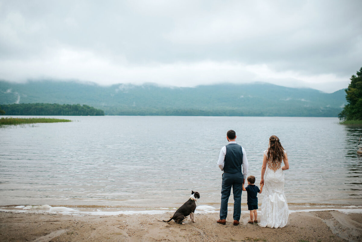bride and groom with child and dog stand on the beach at mountain top inn wedding