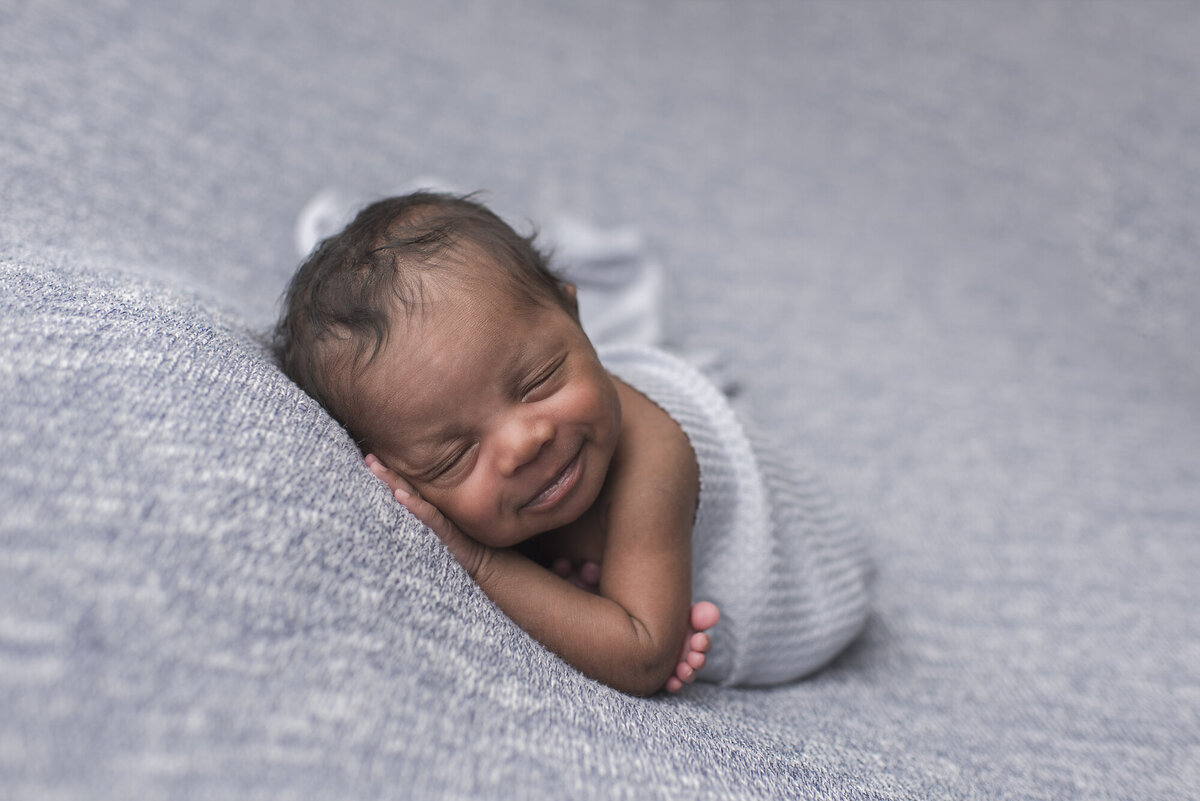 boy baby wrapped in light blue blanket and backdrop behind him in studio