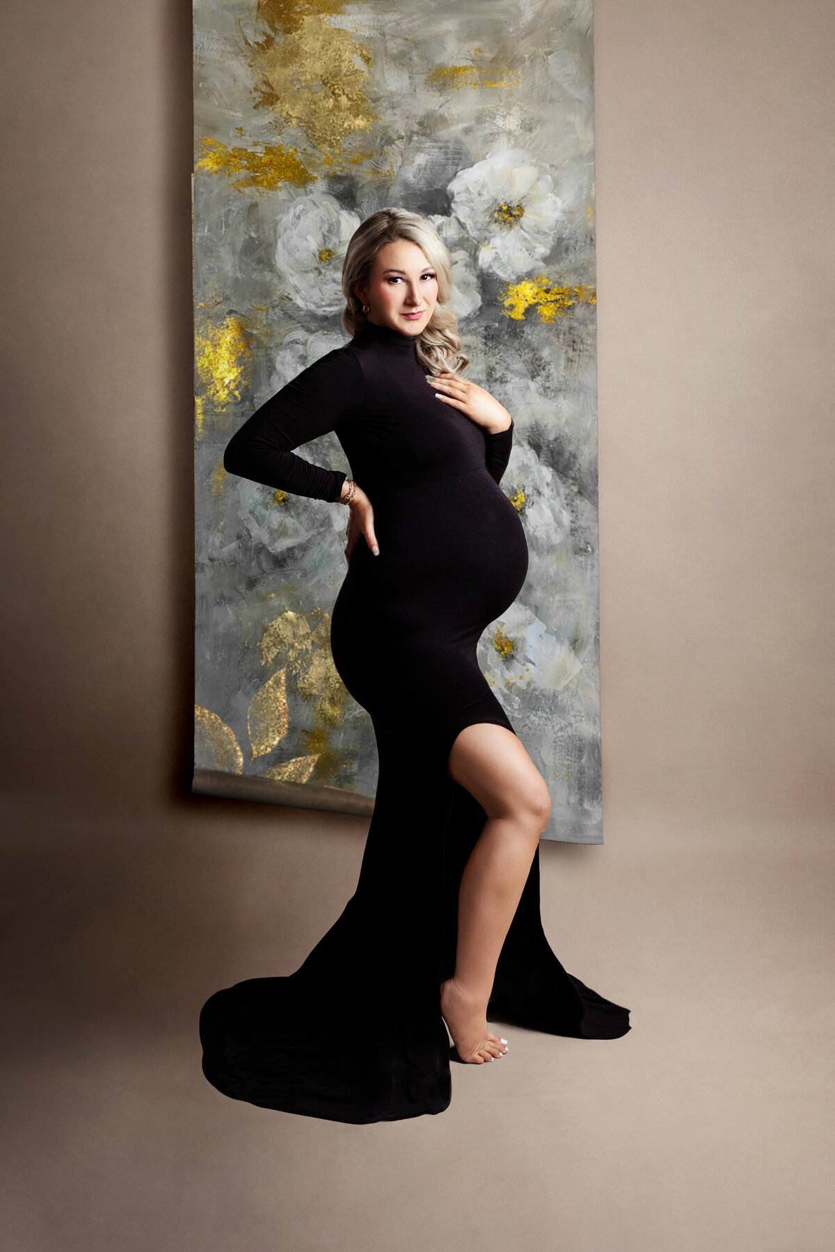 pregnant mother wearing a black fitted maternity gown with a grey gold and white skinny canvas backdrop at a maternity photo shoot in northern va