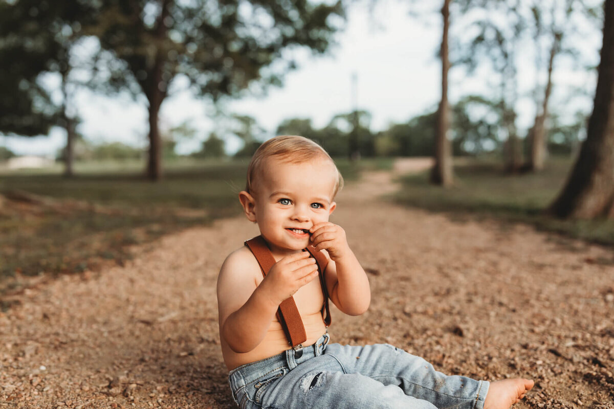 little boy chews on rocks wearing denim pants and suspenders.