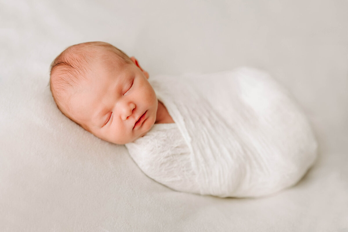 Newborn on white blanket wrapped in white