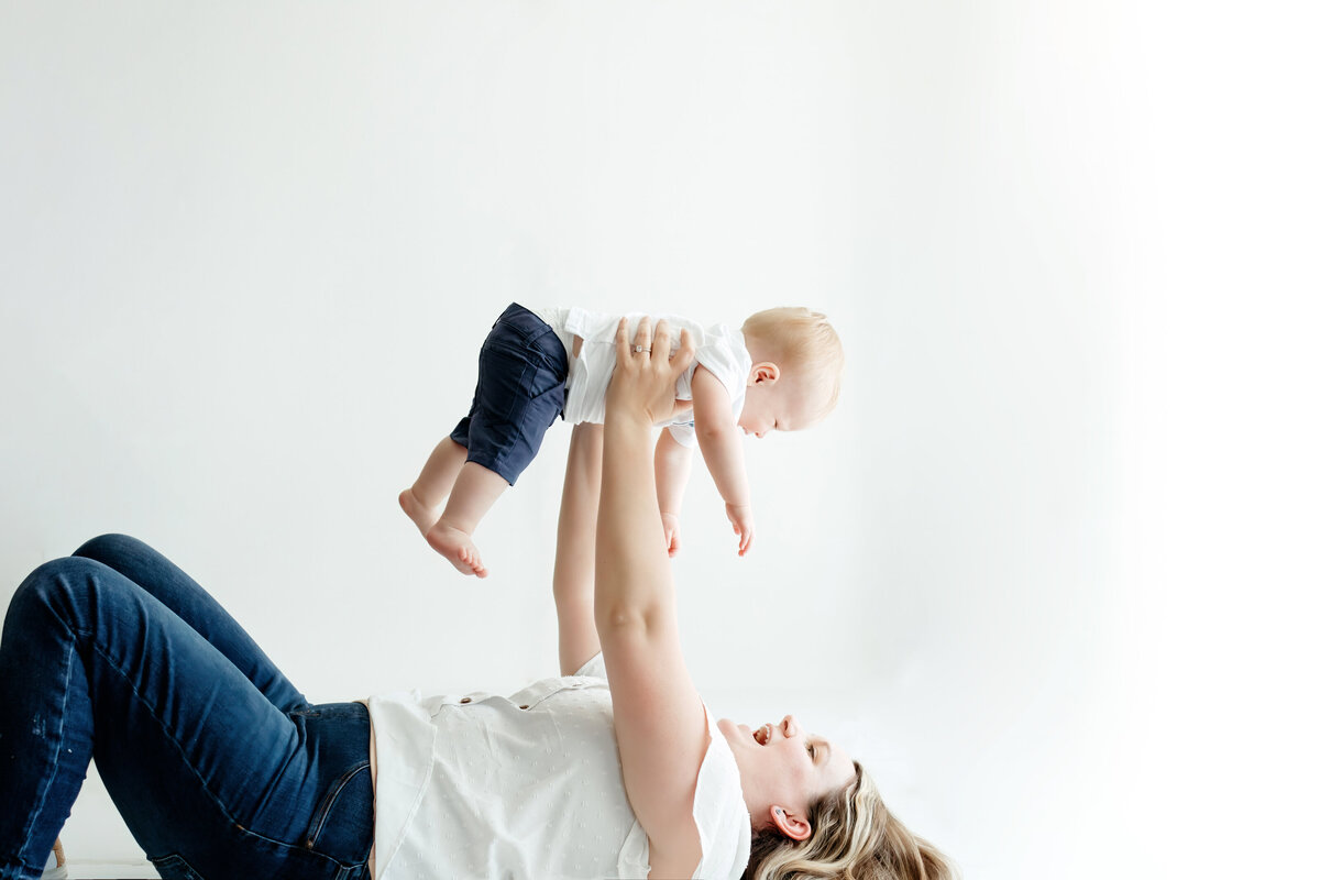 mom holding baby boy up in air while laing on back