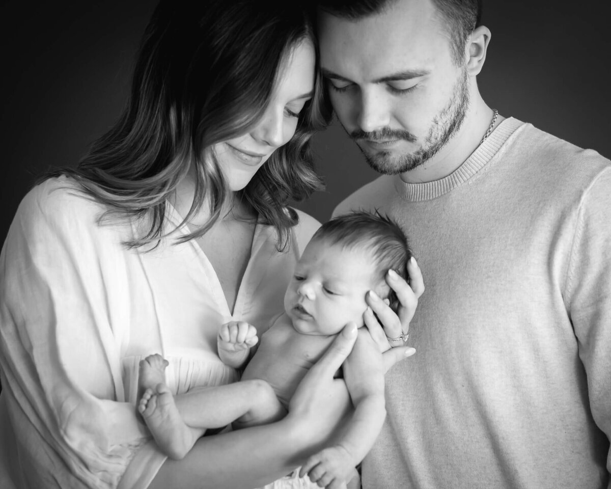 black and white studio protrait captured by Allison Amores Photography parents and newborn huddled close