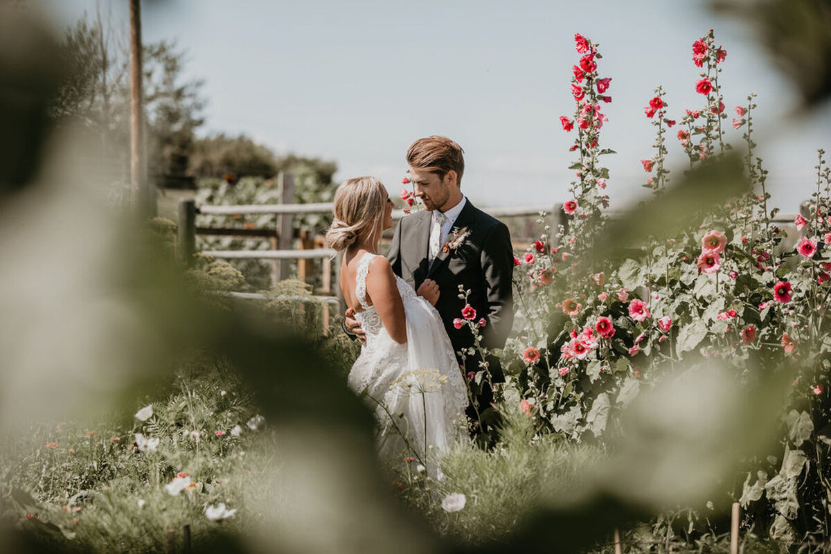 Bride and groom in the flower garden at The Gathered, a nostalgic greenhouse based in Kathryn, Alberta wedding venue, featured on the Brontë Bride Vendor Guide.