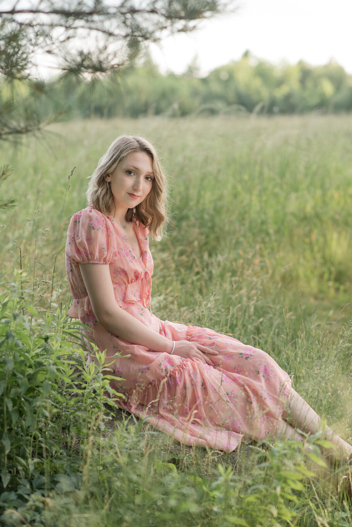 Senior girl in pink dress sitting in field