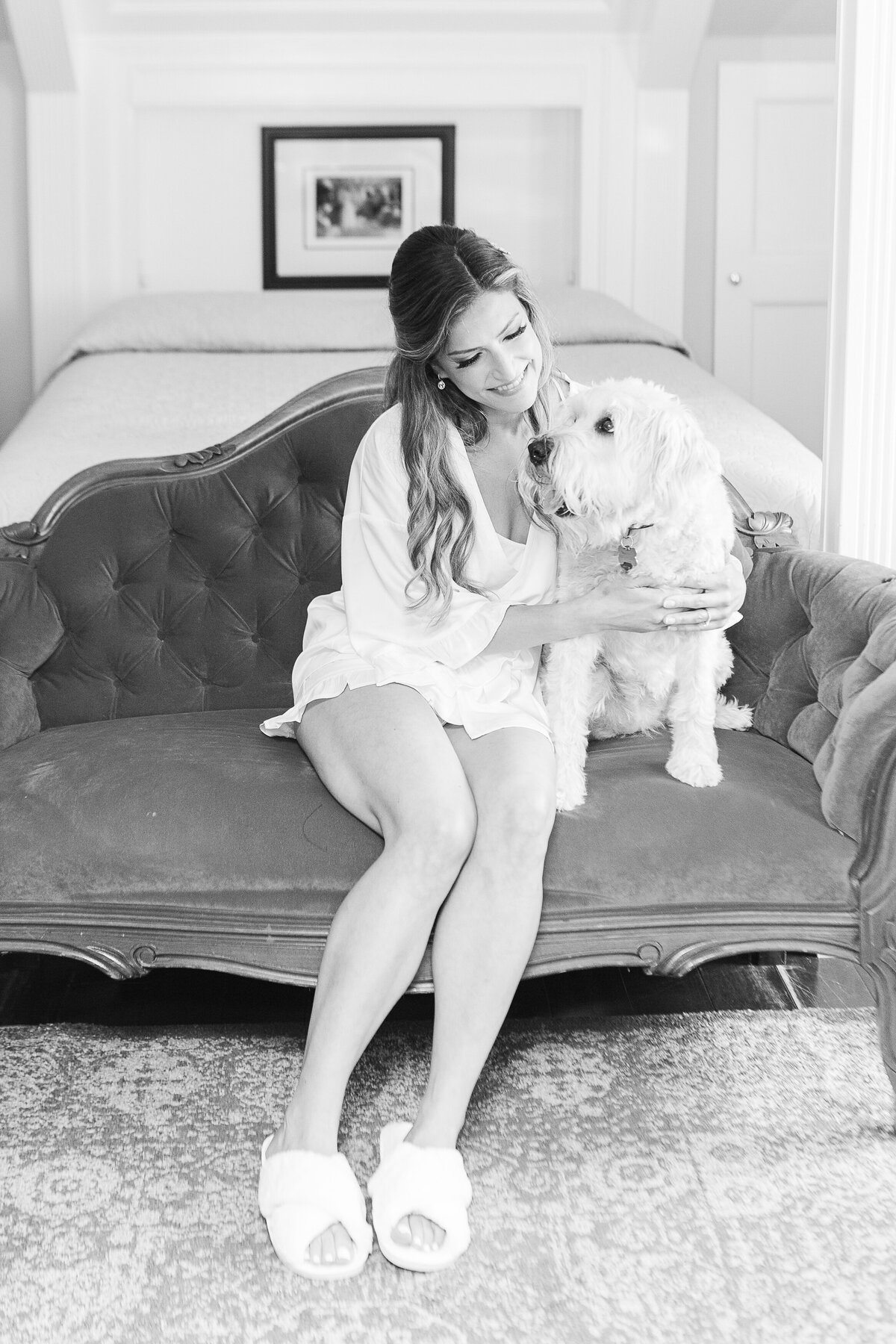 Black and white image. A bride sits on a vintage sofa at the Five Bridge Inn with her pup before her wedding ceremony. Captured by best Massachusetts wedding photographer Lia Rose Weddings.