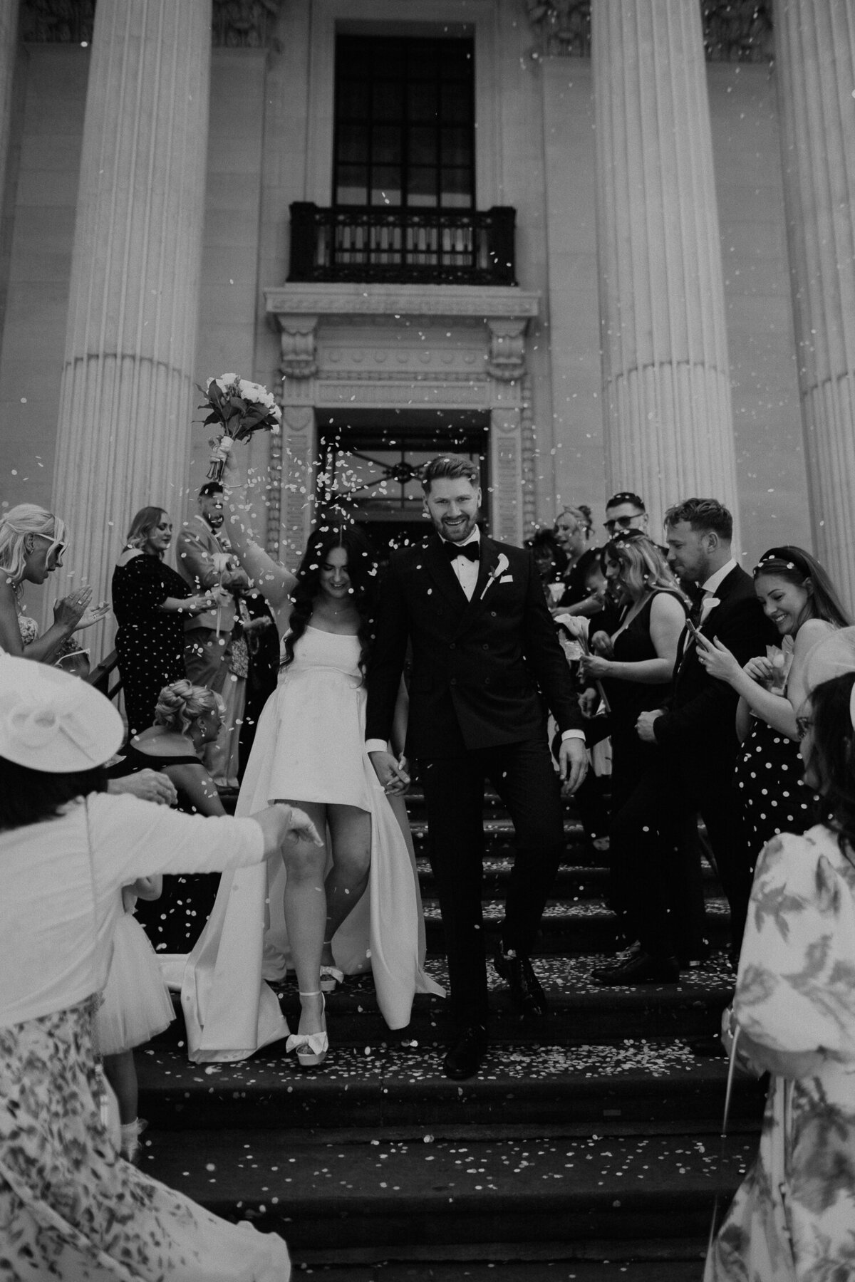 Bride and groom walk down the famous steps of The Old Marylebone Town Hall as their guests throw confetti. 